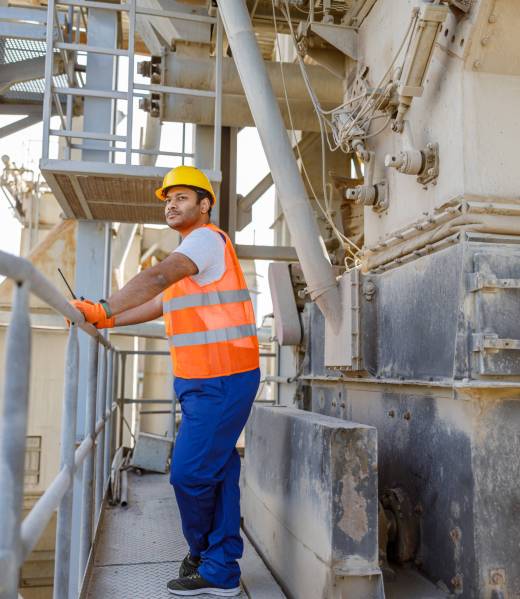 Stern looking manual worker wearing safety equipment, holding walkie-talkie and observing production facility at plant for construction industry production